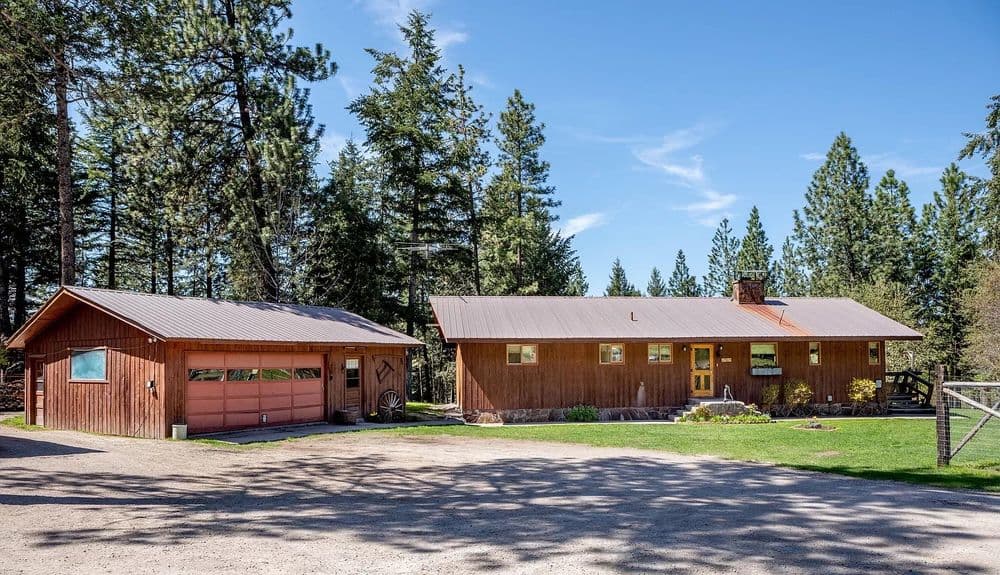 Rustic wooden house with garage surrounded by trees and clear blue sky. Ideal for nature lovers.