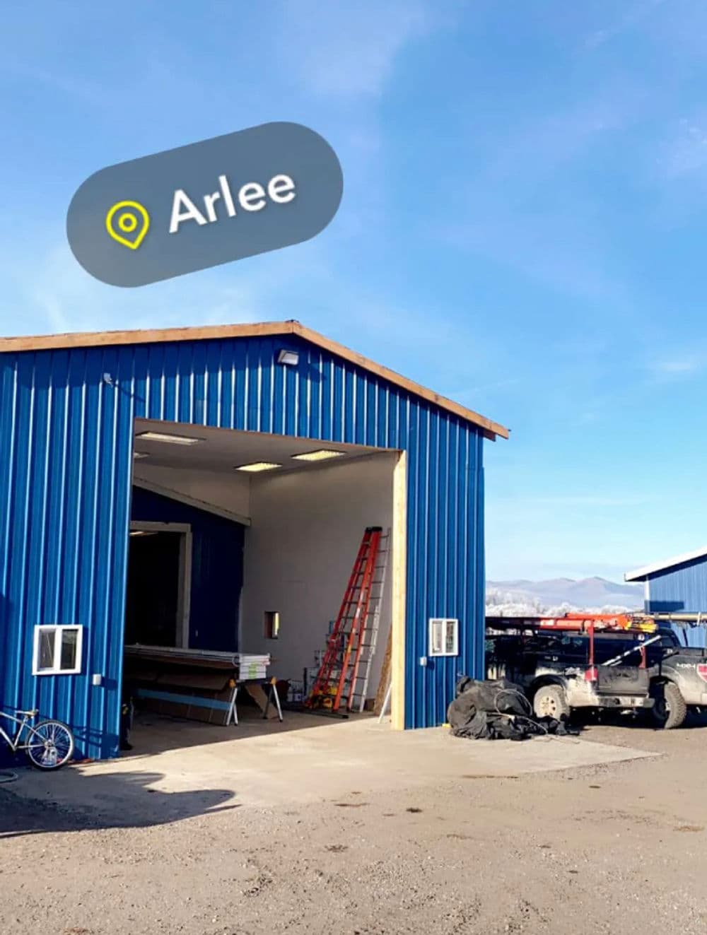 Blue storage building with open door, location pin for Arlee, and ladder visible outside.