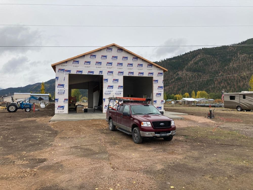 New construction building with a red truck parked in front, surrounded by rural landscape.