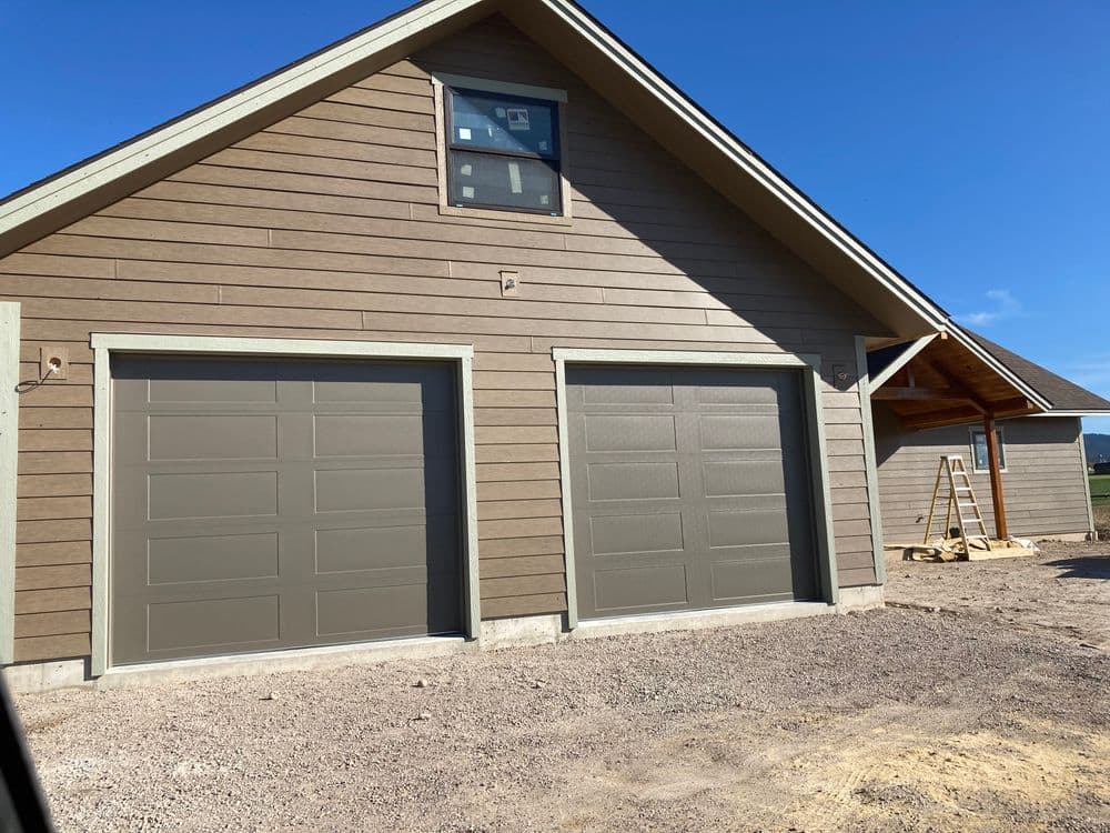 Newly built home with brown garage doors and wooden siding under a clear blue sky.