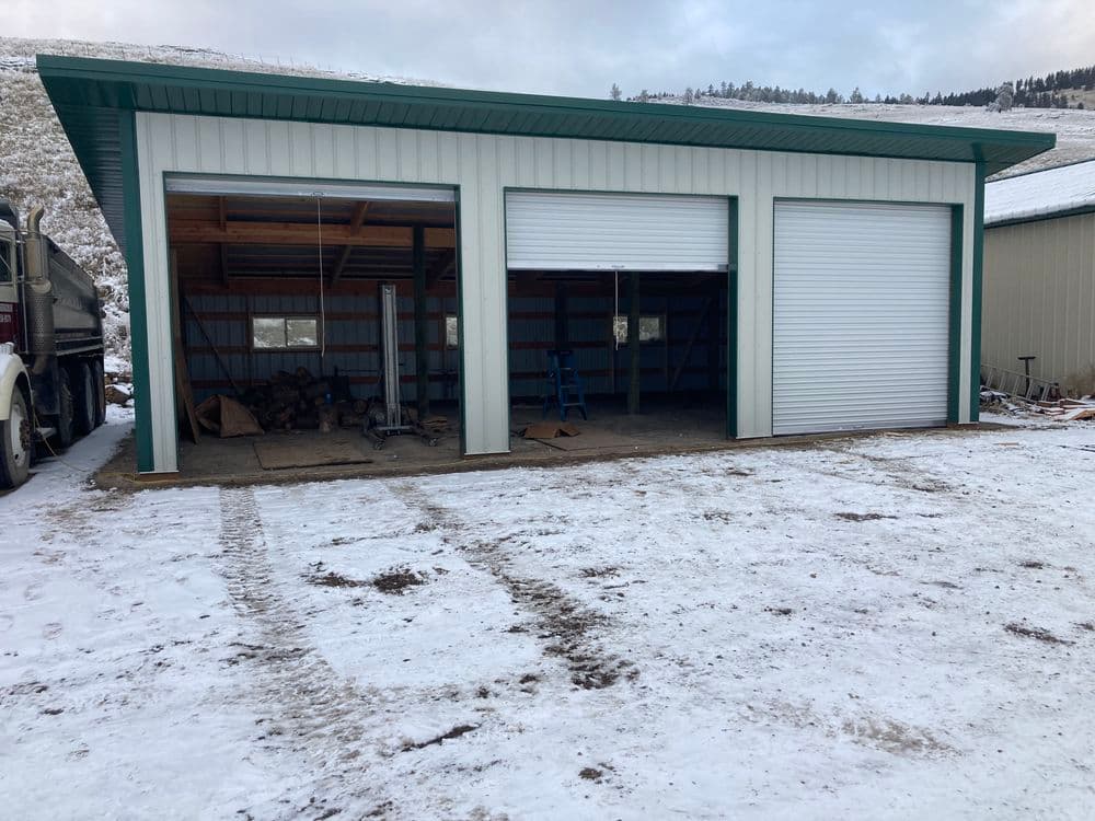 New metal garage with two roll-up doors in snowy landscape, featuring an unfinished interior.