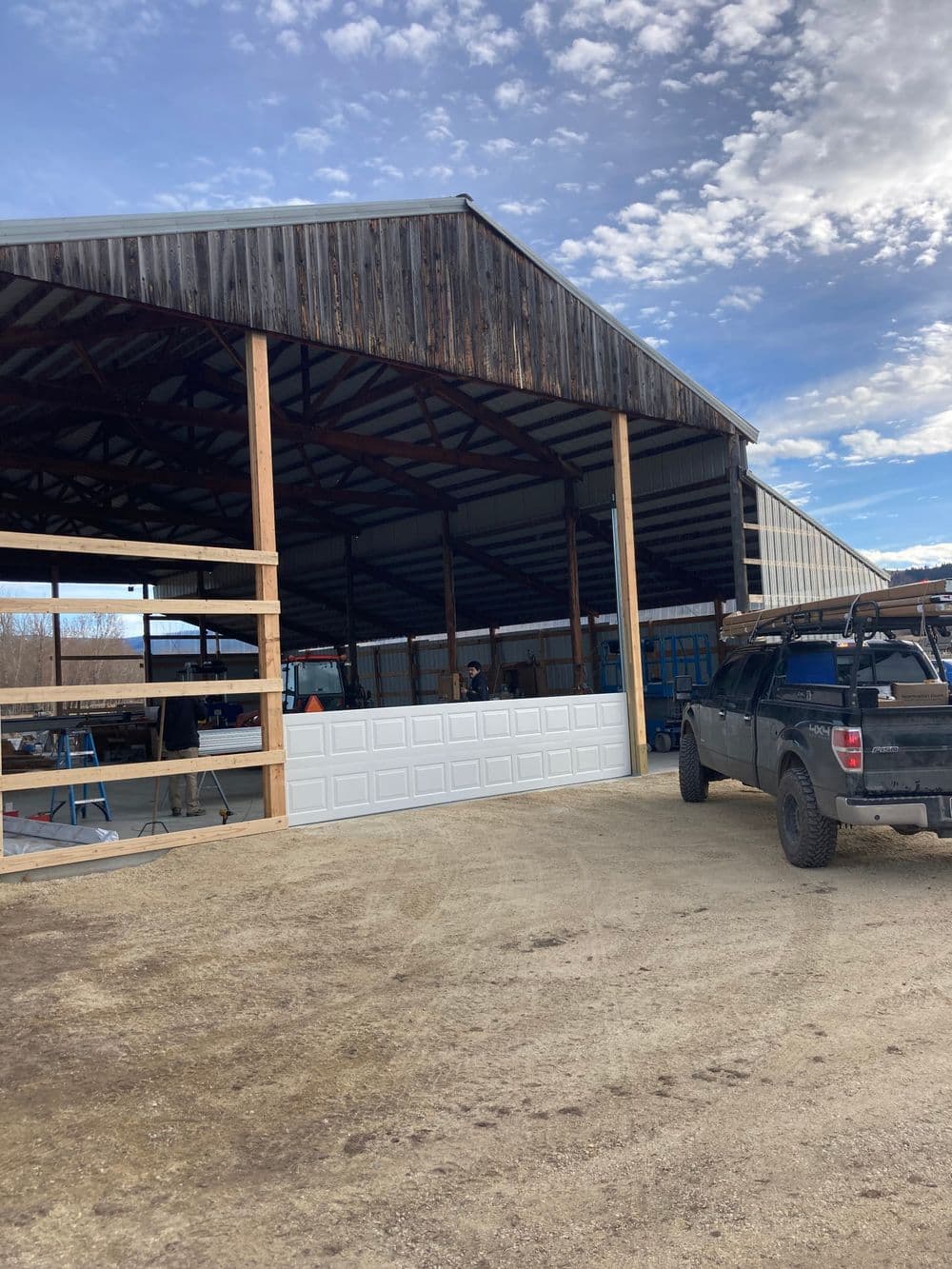 Large open barn with a pickup truck parked outside, featuring wooden beams and clear sky.