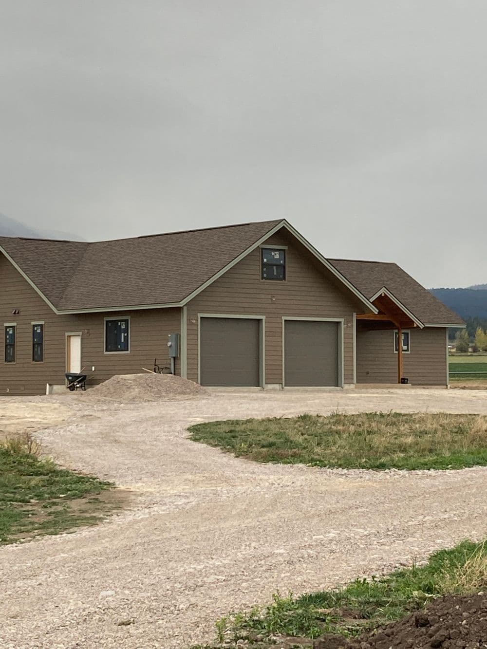 Newly constructed brown house with garage and gravel driveway in a rural setting.