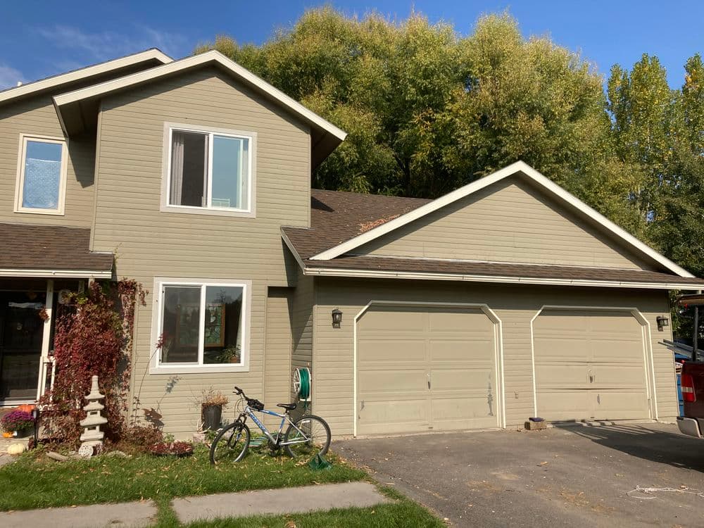 Two-car garage with beige siding and bike outside a suburban house on a sunny day.