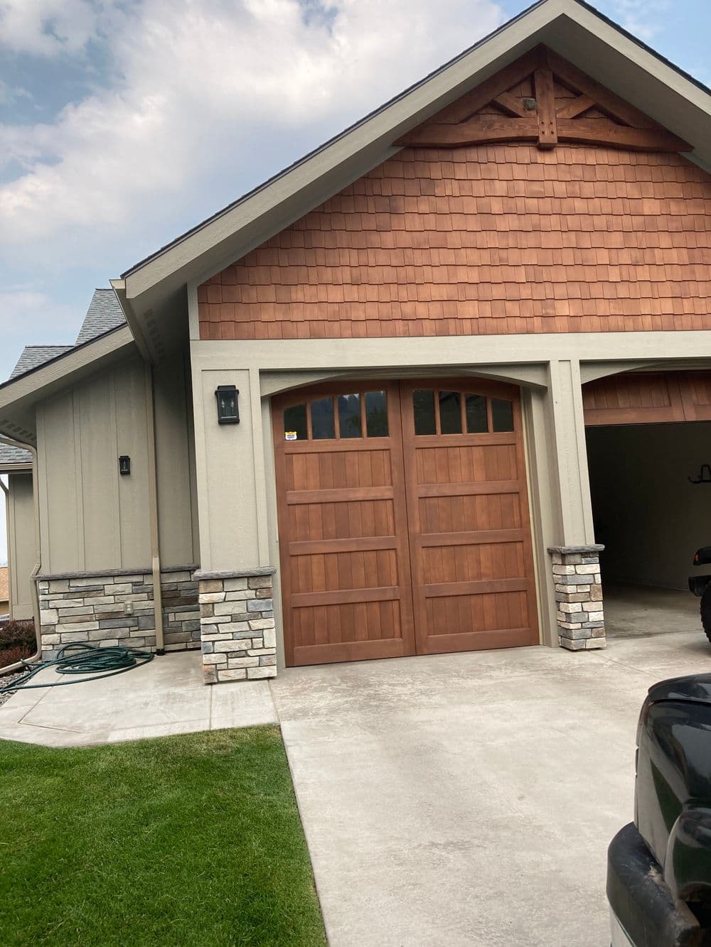 Modern house exterior featuring wooden garage door, stone accents, and landscaped yard.