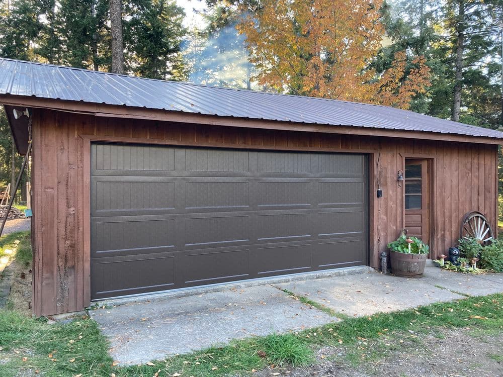 Brown wooden garage with a large door, surrounded by trees and autumn foliage.