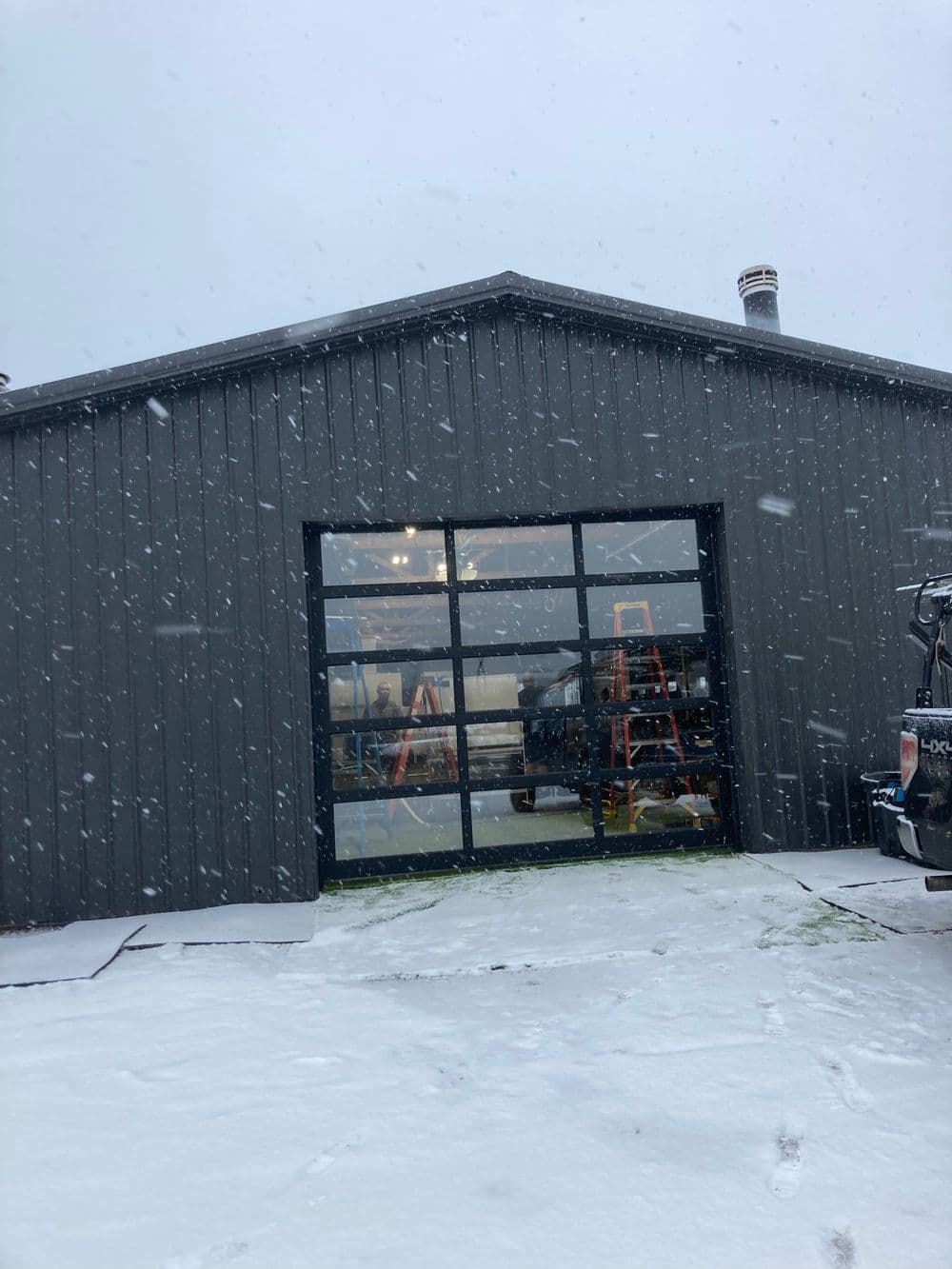 Modern gray garage building in the snow with large glass doors and outdoor equipment visible.