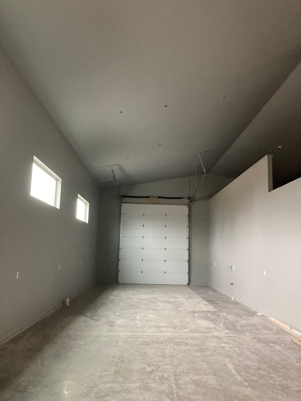 Spacious gray garage interior with large door and windows, ready for customization.