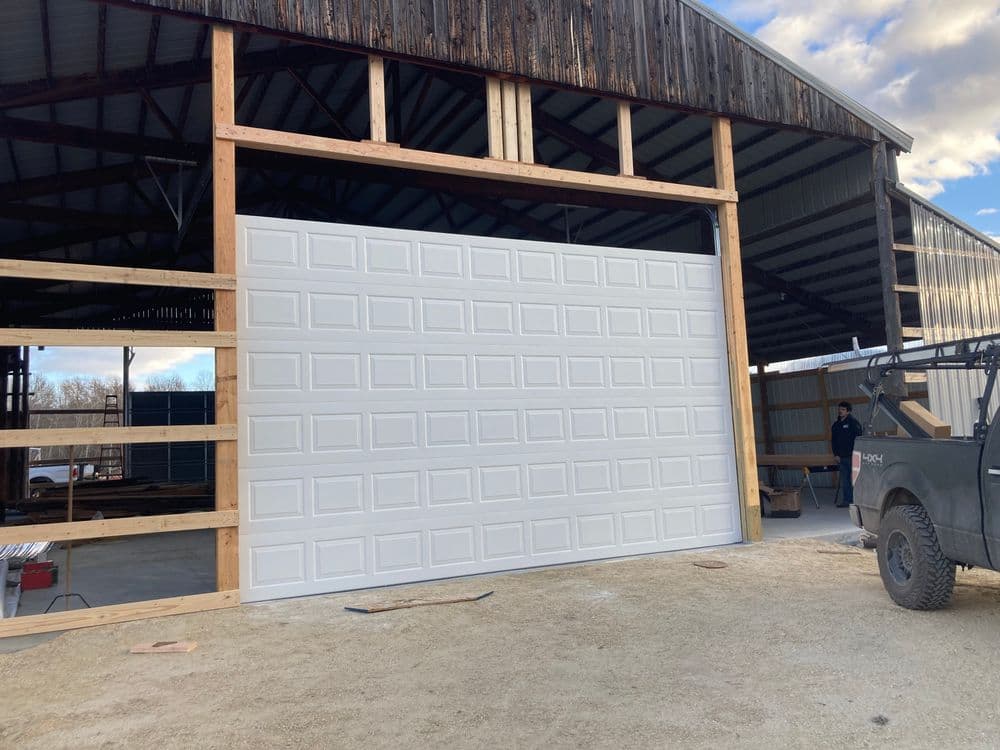 New large white garage door installation in a wooden barn structure under construction.