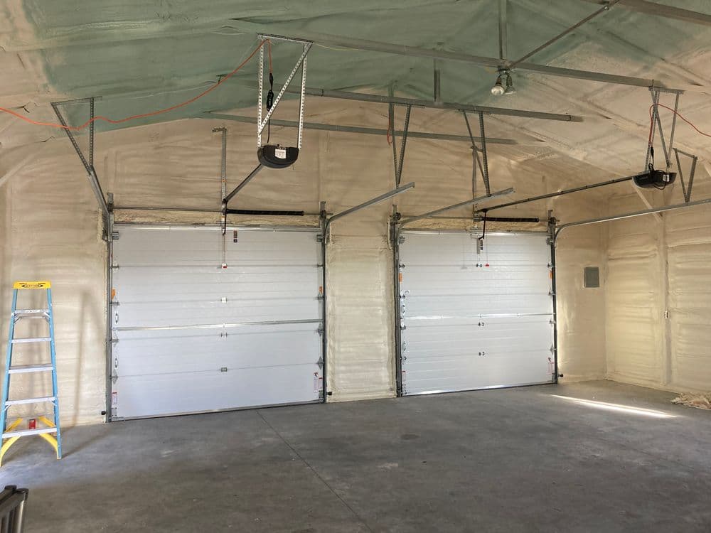 Two newly installed garage doors inside a spacious, unfinished garage with a ladder.