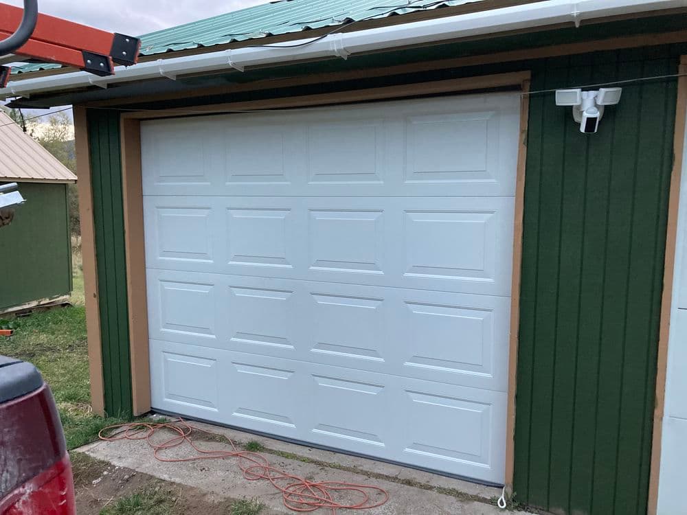 White garage door on a green wooden building, with visible construction tools nearby.