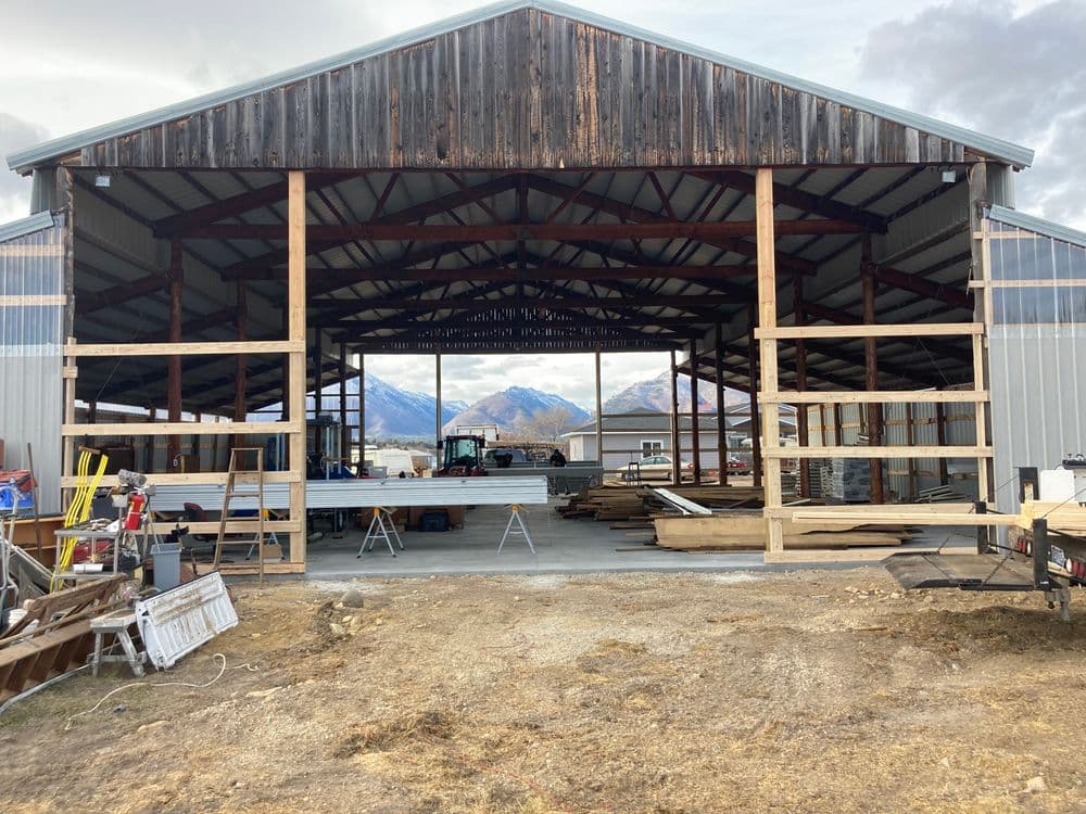 Spacious open barn with wooden beams and mountain backdrop, under construction, showcasing tools.