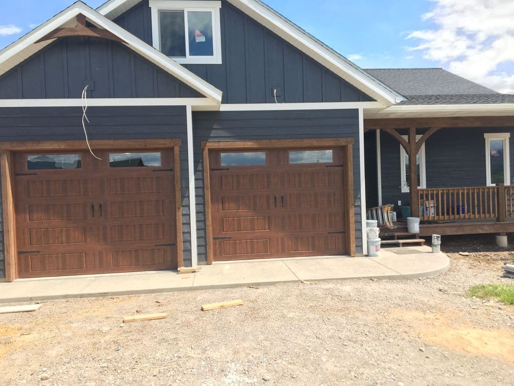 Modern home exterior with dark blue siding, wooden garage doors, and a welcoming front porch.