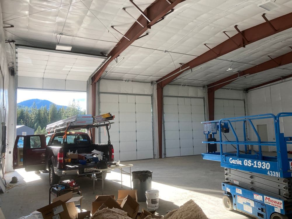 Interior of a spacious industrial warehouse with a truck and lift. Mountain view through doors.