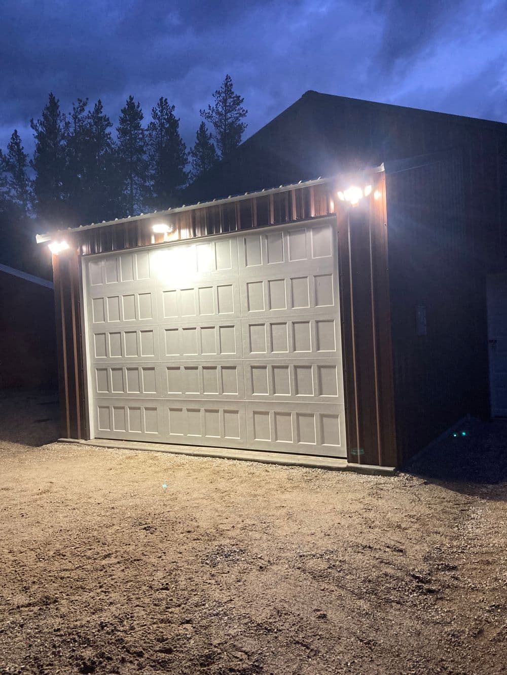 Illuminated garage door on a rustic building at dusk, surrounded by trees.