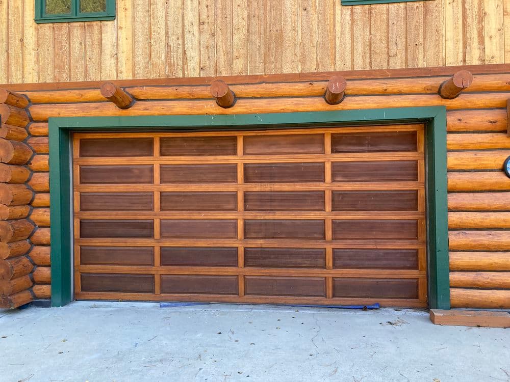 Wooden garage door on a log cabin with green trim and a rustic exterior finish.
