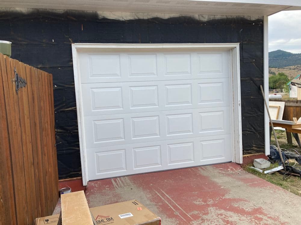 New white garage door installed on a house with wooden fence and construction materials nearby.