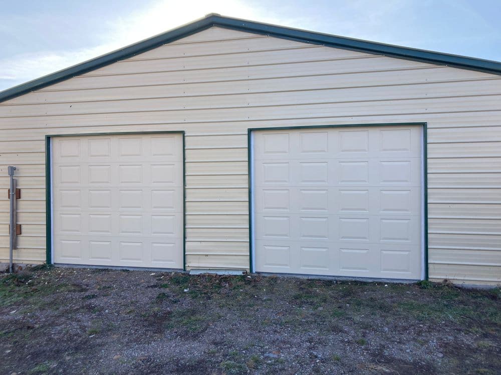 Two white garage doors on a metal building with green trim and a clear sky above.