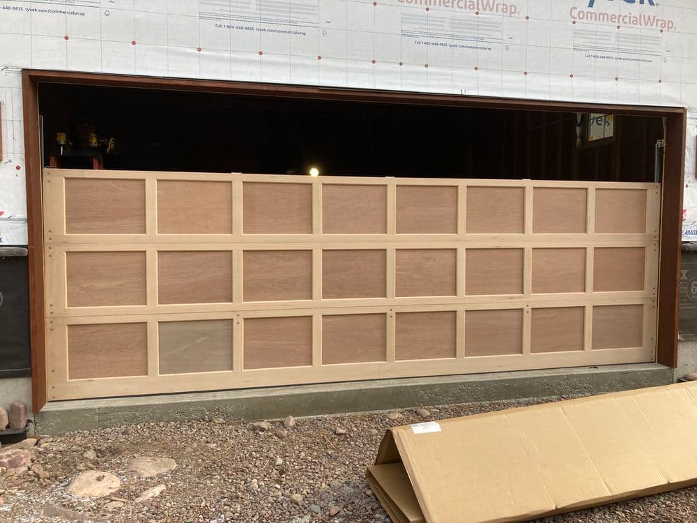 Wooden garage door under construction with framed panels and exposed walls.