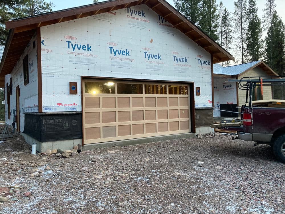 New garage door installation on a home under construction with Tyvek wrap and gravel driveway.