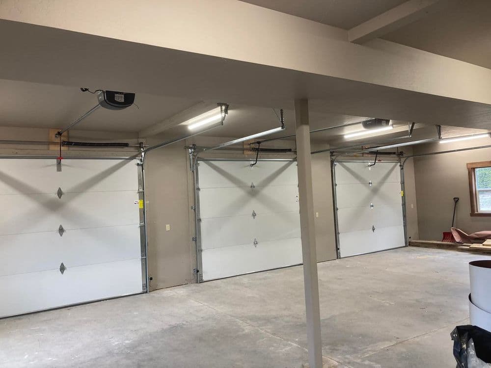Interior view of a garage featuring three white garage doors and overhead lighting.