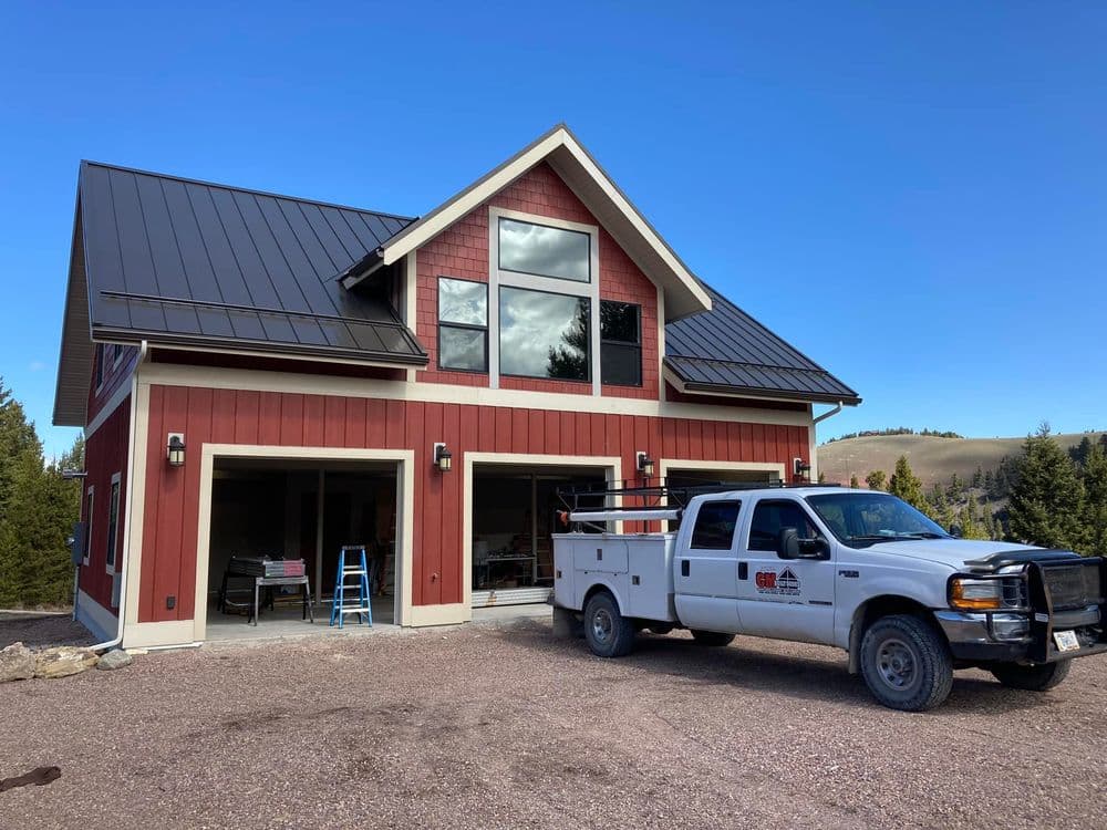 Red house with a metal roof and a work truck parked in front, surrounded by scenic landscape.