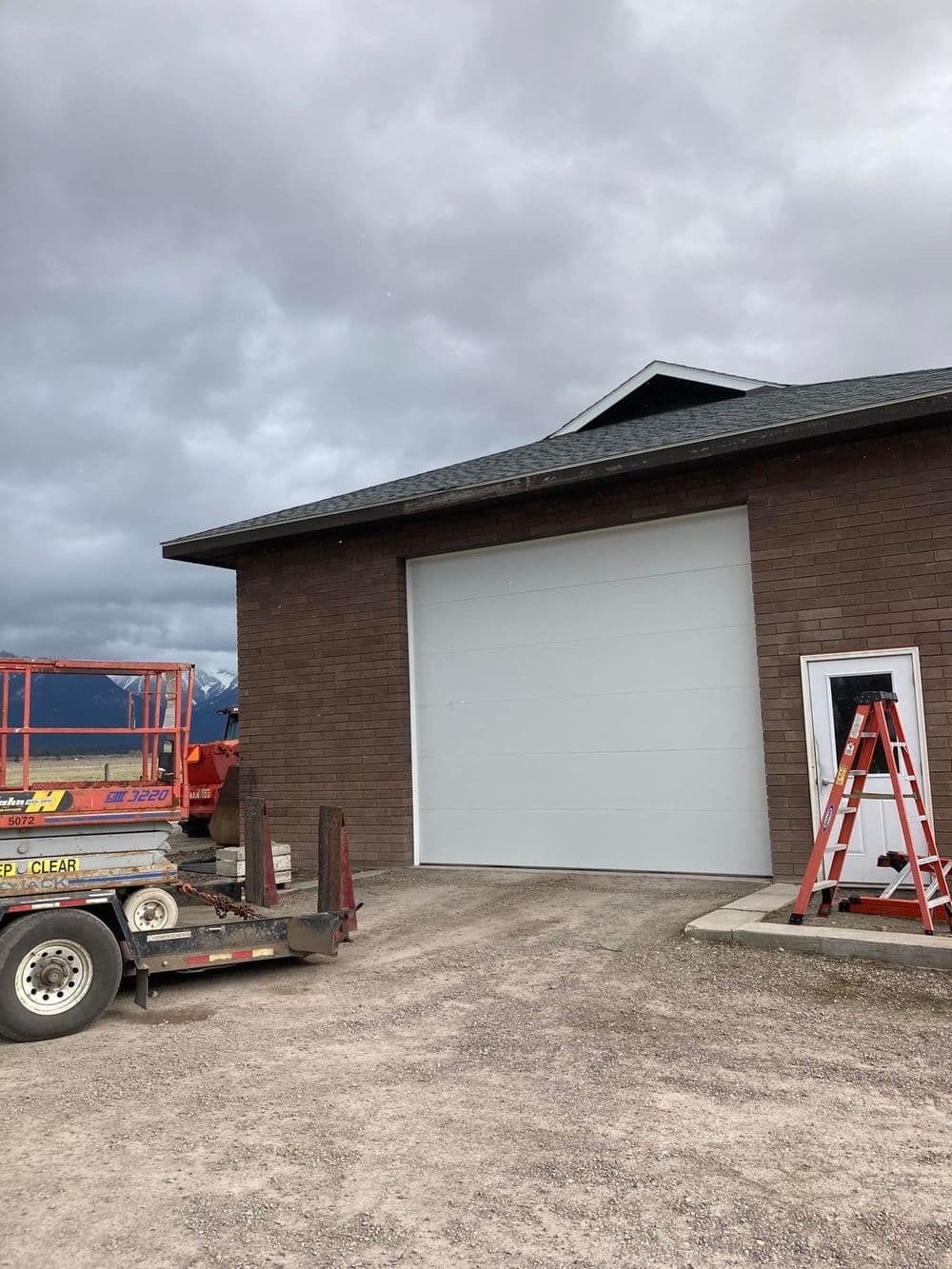 Modern garage with a large door, ladder, and construction equipment under cloudy sky.