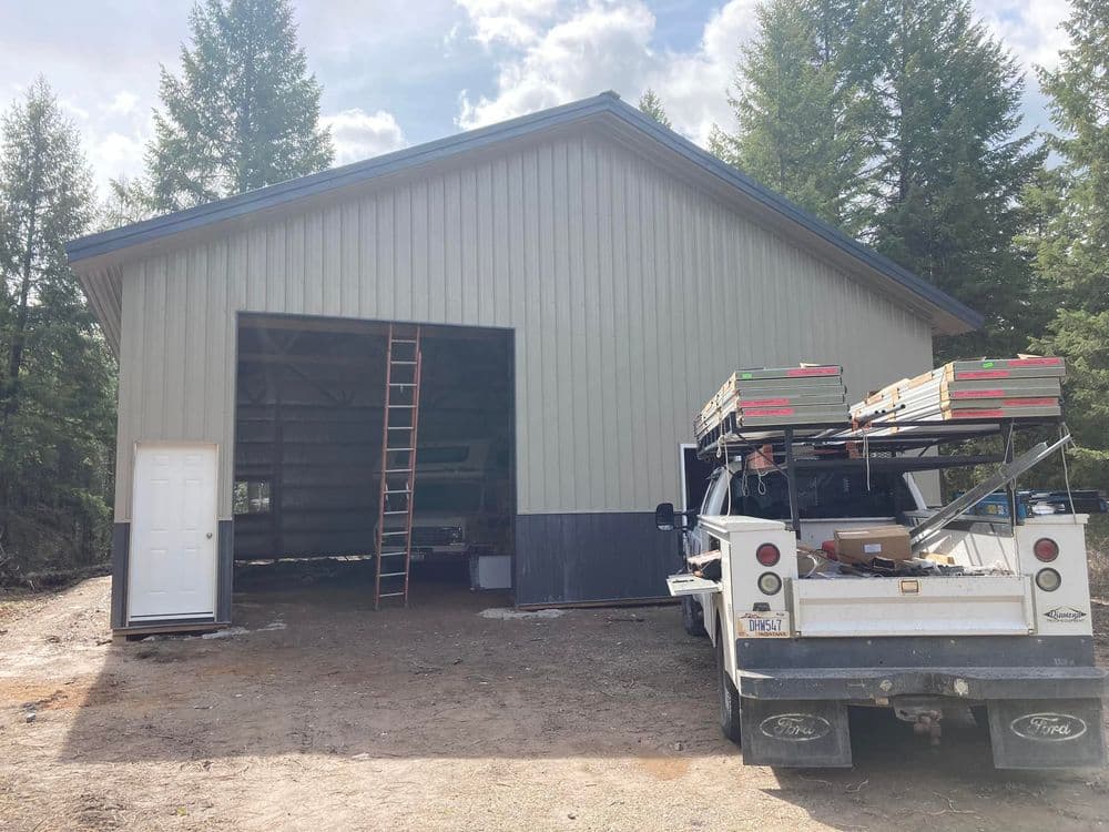 Metal barn with open door, ladder outside, and truck with supplies parked nearby.