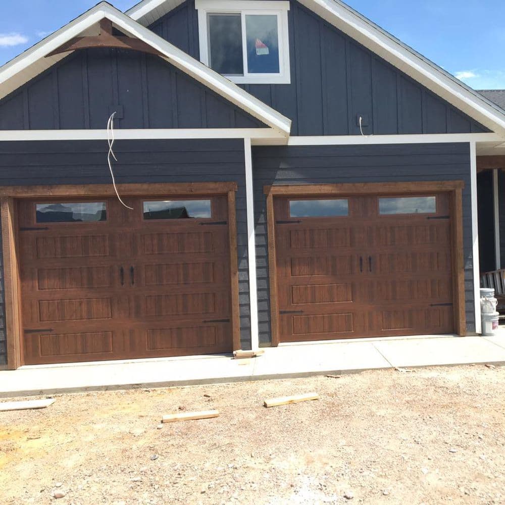 Modern home with two wooden garage doors and blue siding, featuring large windows above.