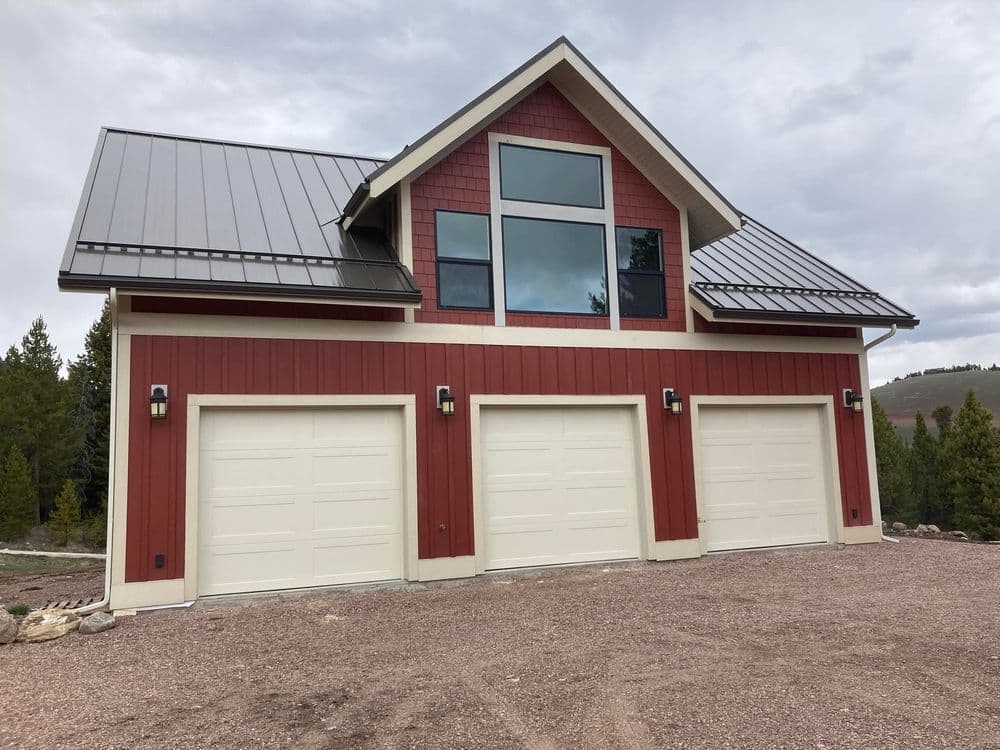Modern red and beige house with three garage doors, large windows, and a metal roof.