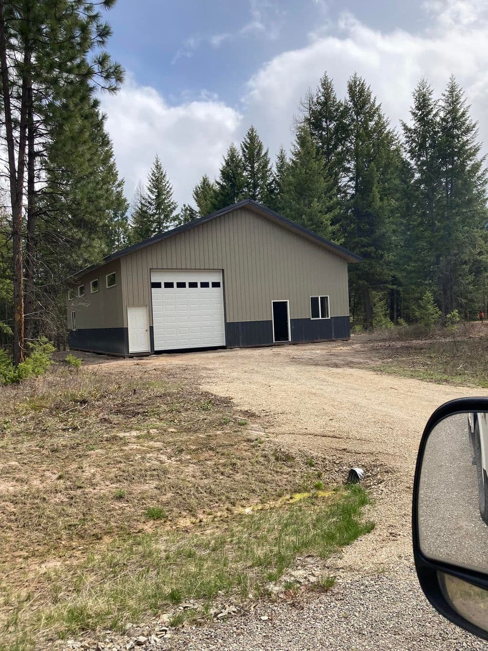 Metal storage building surrounded by trees on a dirt path in a rural setting.